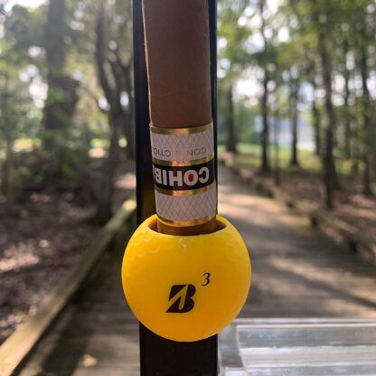 Yellow Bridgestone Cigar Ball holding a Cohiba Connecticut cigar riding over a wooden bridge.